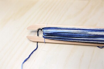 isolated wood shuttle of a loom with blue wool yarn on pale wooden table