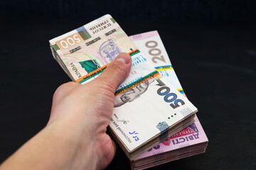 two bundles of hryvnia in a female hand on a black wooden background.