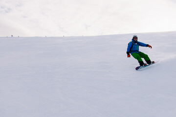 Fototapeta na wymiar A guy in a bright suit rides a freeride on a snowboard on a snowy slope