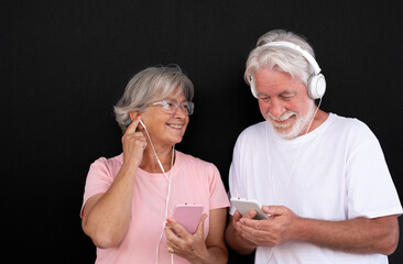 Attractive white-haired senior couple using smartphone with earphones. Two happy retirees enjoying free time and technology, new young people. Black background - Powered by Adobe