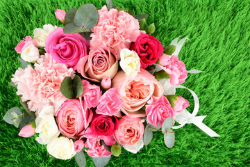A bouquet of roses and carnations tied with a white ribbon stands on the green grass.