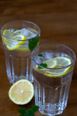 glass of water with lime. Two glass with lemonade or mojito cocktail with lemon and mint. cold refreshing drink or water with ice on rustic wood background. Copy space. vertical. summer drinks.