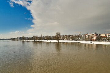 Heidelberg, Germany - Gray clouds covering blue sky over snow covered Neckar riverbank in winter