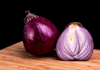 One and a half red onions on a cutting board with a black background