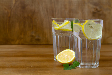 glass of water with lemon. homemade cold refreshing drink or water with ice on rustic wood background. Copy space. summer drinks. Two glass with lemonade or mojito cocktail with lemon and mint.