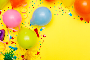 Colorful balloons and confetti on yellow table top view. Festive or party background. Flat lay style. Birthday greeting card. Carnival.