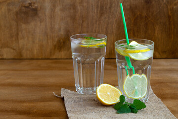 mojito cocktail with lime.summer drinks. two glasses of lemonade with lemon and fresh leafs mint. homemade cold refreshing drink or water with ice with sackcloth on rustic wood background. Copy space.