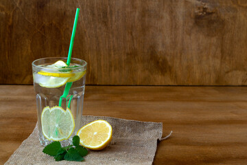 mojito cocktail on wood.summer drinks. glass of lemonade with lemon and fresh leafs mint. homemade cold refreshing drink or water with ice with sackcloth on rustic wood background. Copy space.