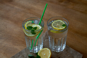 Fototapeta premium mojito cocktail with lime.summer drinks. glass of lemonade with lemon and fresh leafs mint. homemade cold refreshing drink or water with ice with sackcloth on rustic wood background. top view
