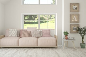 Fototapeta premium White living room with sofa and summer landscape in window. Scandinavian interior design. 3D illustration