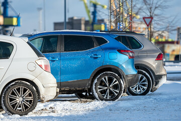 row of different cars parked  in the outdoor parking on a snowy winter day