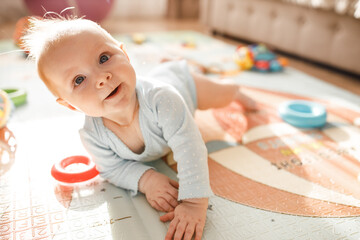 Wonderful baby girl laying on colourful mat at home. Adorable cute joyful toddler playing in kids room, smiling, childhood and childcare concept