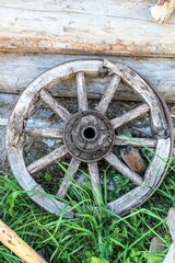 Fototapeta na wymiar An old cart wheel against the wall of a log house.