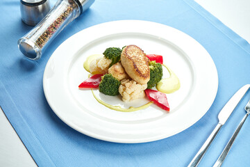 Diet turkey cutlets garnished with steamed vegetables in a white plate on a blue tablecloth.
