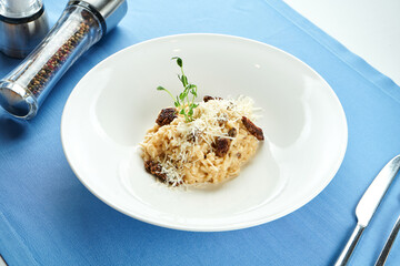 Classic Italian risotto with truffle and sun-dried tomatoes, parmesan cheese in a white plate on a blue tablecloth.