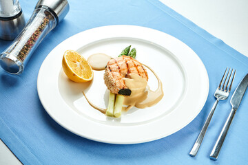 Appetizing salmon steak with asparagus and sauce in a white plate on a blue tablecloth.