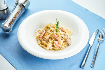 Classic, homemade Italian pasta (spaghetti) in cheese sauce with with shrimps and seafood in a white plate on a blue tablecloth