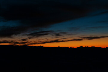 silhouettes of a mountain range against a dark sky with orange flowers at sunset