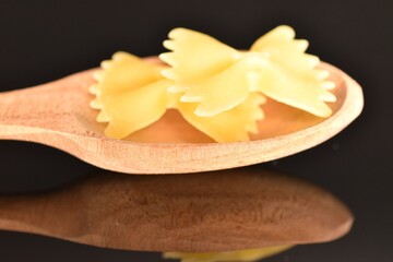 Several yellow pasta, in the shape of a butterfly in a wooden spoon, close-up, isolated on black.