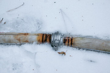 Winter. Everything is covered with snow. Leak in the connection of pipes pumping water out of the...