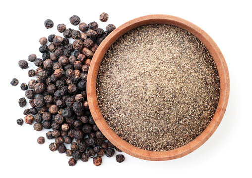 Ground black pepper in a wooden bowl and peppercorns on a white background, isolated. Top view
