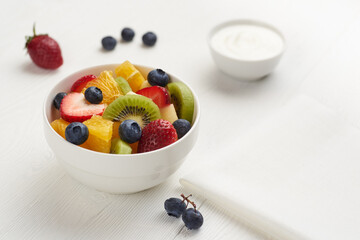 Fruit salad in a white painted wooden table with berry, yoghurt  and napkin with copy space.