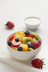 Fruit salad in a white painted wooden table with berry, kiwi, yoghurt  and napkin with copy space.