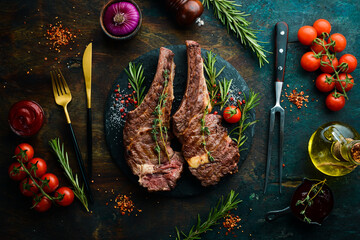 Two veal steaks on the bone with spices, thyme and rosemary. Barbecue meat. Top view. Flat lay top view on black stone cutting table.