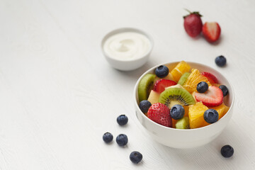 Fruit salad in a white painted wooden table with berry, kiwi, yoghurt with copy space.