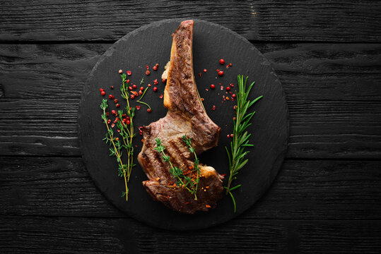 Veal steak on the bone with spices, thyme and rosemary. Top view. Flat lay top view on black stone cutting table.