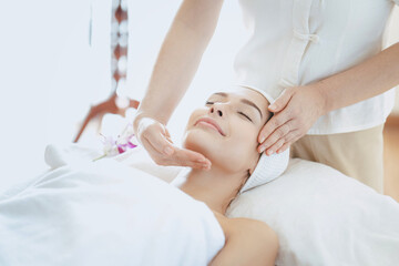 Obraz premium Female massage therapist giving a massage at a spa. Young woman receiving head and facial massage in spa salon.