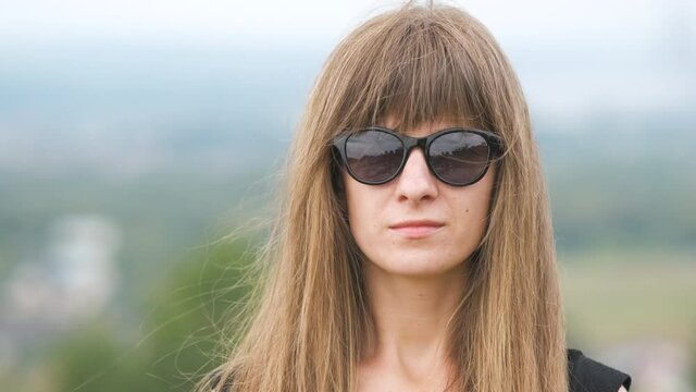 Portrait of a young long haired woman in dark sunglasses looking in camera on a windy summer day.