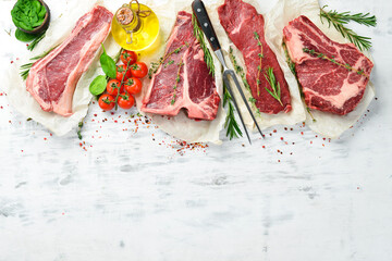 Set of raw steaks: t-bone, striploin, Rib eye, new york steak. Top view. On a white wooden...