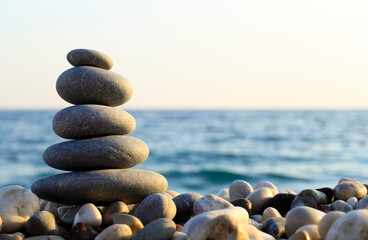 Balanced Pebbles Pyramid  on the Beach on Sunny Day and Clear Sky at Sunset. Blue Sea on Background