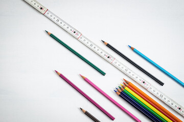 Creative background expressing the concept of distancing at school, coloured crayons and a wooden meter are resting on a white background.