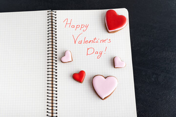 Inscription in notebook Happy Valentines Day, close up and cookies in shape of hearts.