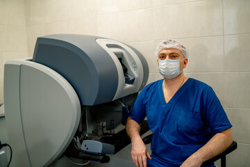 Doctor in mask sits near controll distance equipment for robotic machine. Modern futuristic machine...