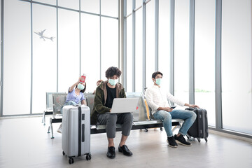 Asian young tourist wear face mask keep distance away from each other to prevent covid19 infection, online working on computer, waiting airline flight at airport terminal, red cross shows on empty cha