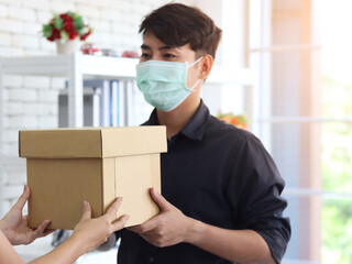 Hands deliver the goods to the recipient customer. Young man wearing face mask receiving delivery...