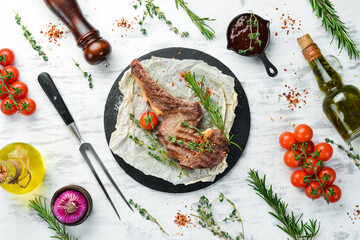 Grilled Beef steak on the bone with spices and vegetables on a white wooden background. Flat lay. Top view.