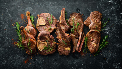 Set of grilled steaks on a black stone table with spices and herbs. Top view. Free space for your...