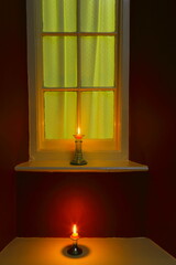 Two candles burning near window