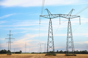 High voltage towers with electricity transmission power lines in field on sunny day