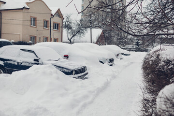 Fototapeta na wymiar Parked cars covered with snow during snowfall in city. Automobiles stuck in heaps after winter blizzard