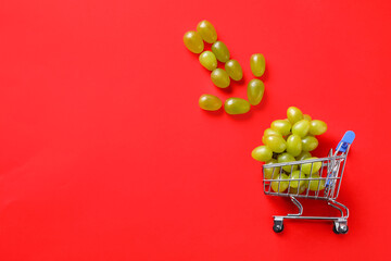 Arrow made of grapes pointing at small shopping cart with berries on red background, flat lay....