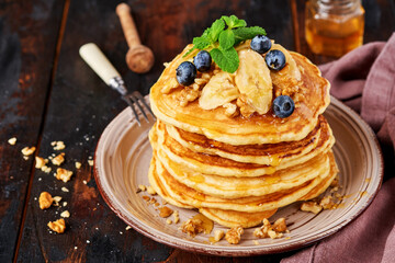 Pancakes with banana, walnut, honey and caramel for a breakfast on dark wooden background. Selective focus.