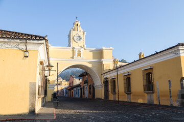 Famous Santa Catalina Arch and colonial houses in main avenue of Antigua Guatemala - colorful yellow arch of colonial city in Guatemala early in the morning