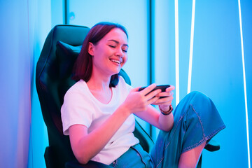 Young female professional cybersport gamer play mobile game by smartphone on eSport tournament online in colorful neon lights room. © romankosolapov