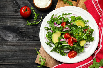 Delicious salad with avocado, arugula and tomatoes on black wooden table, flat lay