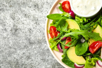 Delicious salad with tomatoes, arugula and avocado on grey table, top view. Space for text